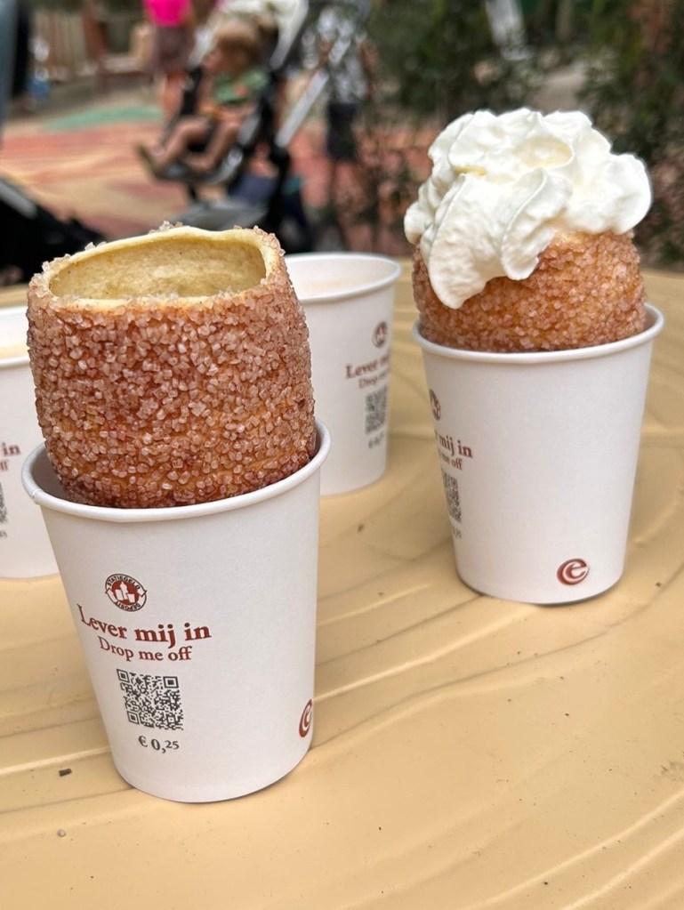 Sugar-coated chimney cakes with whipped cream served in cups at a theme park.